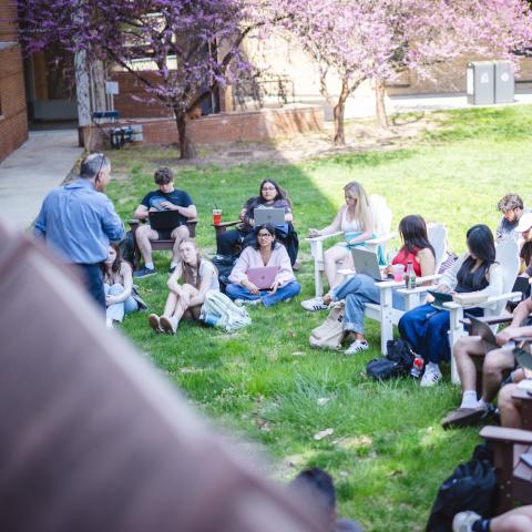 Students sit outside on a spring day to listen to a lecture.